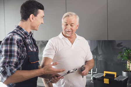 Two men of plumbers stand in the kitchen and choose a tool for work. Each of them holds a power key in hands.の写真素材