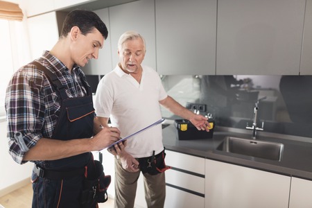 Two men of plumbers are standing in the kitchen. An elderly man inspects the place of repair work.の写真素材