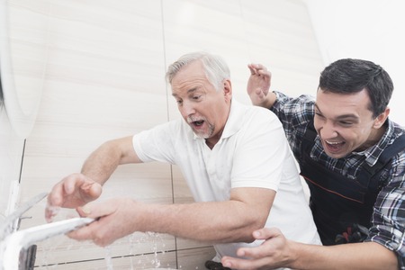Two plumbers repair the faucet in the bathroom. They have a big tap and they are having fun.の写真素材