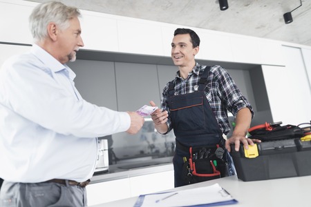 A plumber man communicates with a client who pays for the work done. The old man gives the plumber a fee.の写真素材