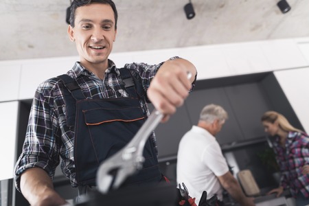 The plumber is posing in the kitchen. He holds a wrench in his hands and smiles.の写真素材