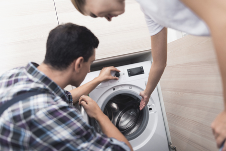 The woman called the repairman of the washing machine. She, along with the master, examines the washing machine.の写真素材