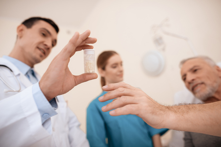 The old man lies on a cot in the medical ward, and next to him there is a doctor and a nurse.の写真素材