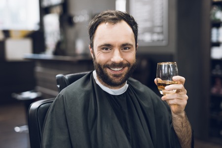 A man drinks alcohol in the hairdressers armchair of a modern barbershop.の写真素材