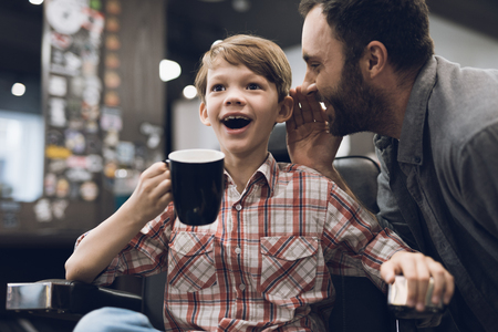 The boy listens to an adult man sitting in a barbershop hairdressers chair.の写真素材