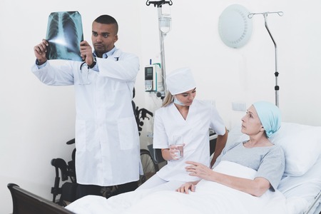 The nurse is sitting next to the patient. The doctor is standing next to a woman with cancer.