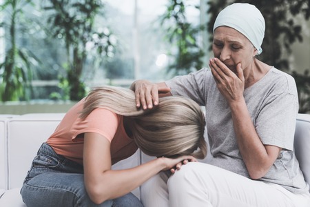 A woman with cancer is sitting on a white sofa in a modern clinic. Next to her sits her daughter.の写真素材