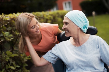 A woman with cancer is sitting in a wheelchair. She walks on the street with her daughter and they...