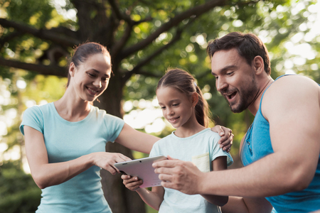 The family rests in the park after playing sports. They are looking at something on the tabletの写真素材