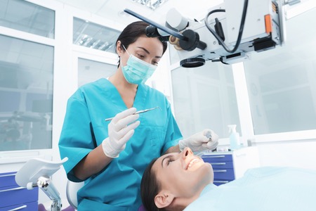 A female dentist is treating a patient. She is sitting on the dental chair. The doctor uses a special dental instrument.の写真素材