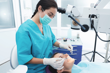 A female dentist is treating a patient. She is sitting on the dental chair. The doctor uses a special dental instrument.の写真素材