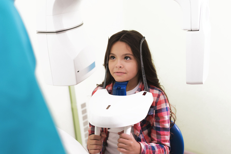 A male doctor makes an x-ray of the girls jaw, which sits in a special X-ray machine. The girl is smiling.の写真素材