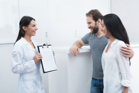A man and a woman came to see a dentist. The receptionist fills in the form and interviews the patients.の写真素材