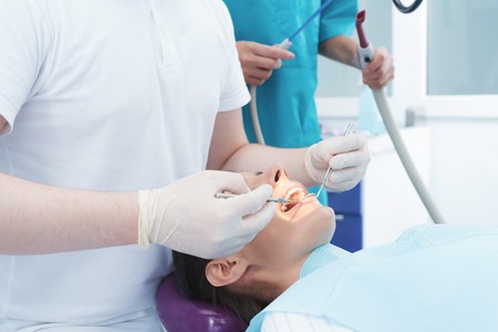 A woman is sitting in a dental chair at a dentists reception. A male doctor is treating the patient teeth.の写真素材