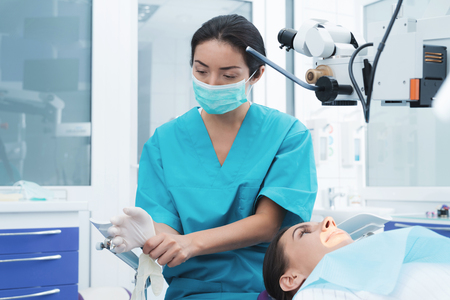 A female dentist is treating a patient. She is sitting on the dental chair. The doctor uses a special dental instrument.の写真素材