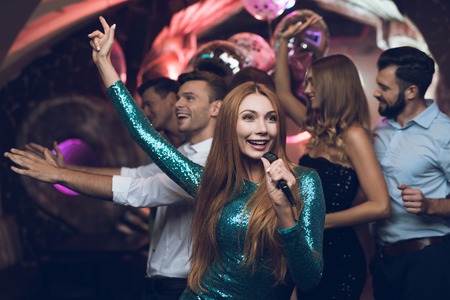 A woman in a green dress is singing songs with her friends at a karaoke club. Her friends have fun on the background.の写真素材