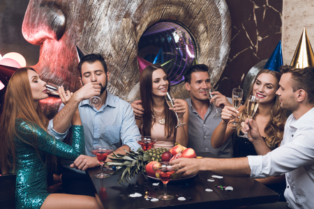 Young people are resting in a trendy nightclub. They clink glasses and drink champagne.