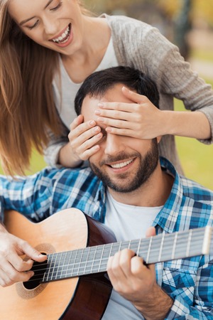 A man on a wheelchair playing guitar in the park. A woman came to him from behind and closed her eyes with her hands.の写真素材