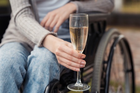 Close up. A woman in a wheelchair in the park holds a glass of champagne in her hands.の写真素材