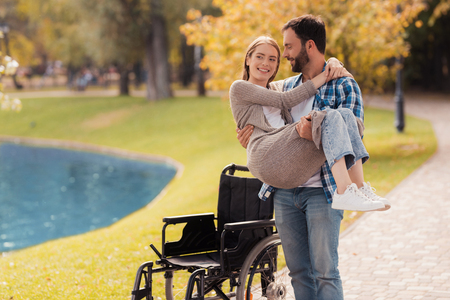 The man is holding a woman. Behind them is a wheelchair. A man and a woman are smiling.の写真素材