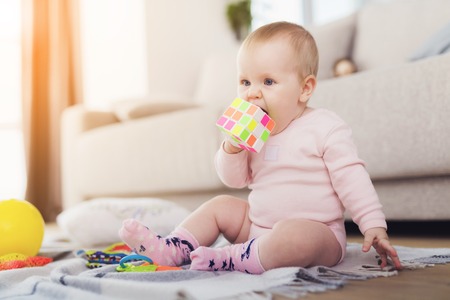 A small beautiful baby sits on the floor and plays with bright, flowery toys.の写真素材