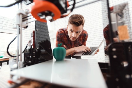 A man with a laptop in his hands controls the process of printing a 3d printer. 3d printer has...