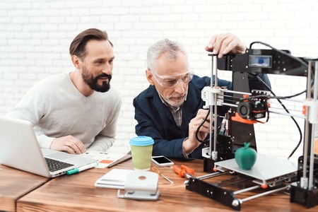Two engineers print the details on the 3d printer. An elderly man controls the process.の写真素材