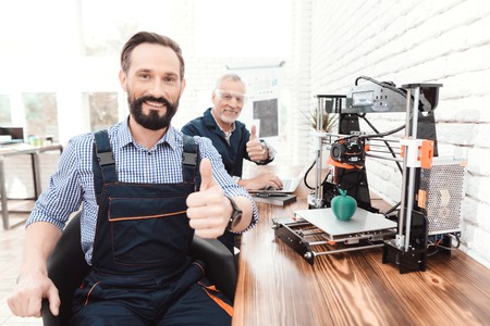 An engineer in a working overall posing in a technical laboratory. Behind it is a 3d printer.の写真素材
