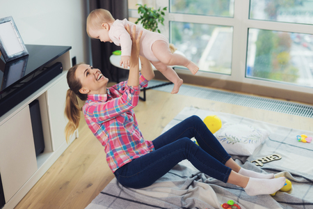A woman in a pink shirt sits on the floor in the living room and holds her child in her arms. The child is happy.の写真素材