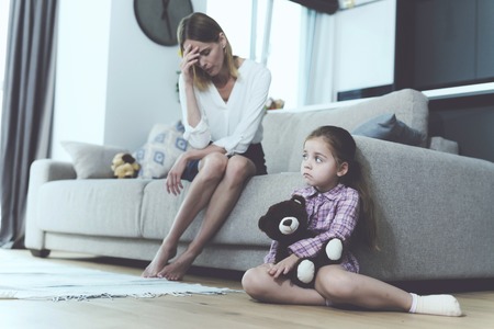 The woman is talking to a small offended girl, who sits next to the sofa and holds a toy in her hands.の写真素材