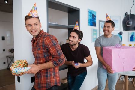 Men in birthday hats are preparing a surprise birthday party. They are preparing to meet the...