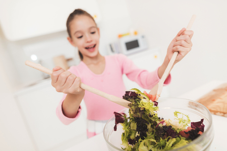 The girl is learning to prepare a salad in a light kitchen.の写真素材