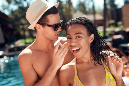 The guy is talking in the ear of a girl, sitting together by the pool at a party.の写真素材