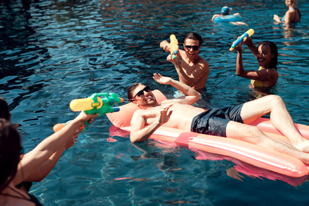 Friends are playing with water guns, standing in the water in the pool.の写真素材