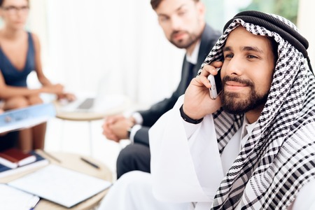 An arab businessman talks on the phone while discussing a business deal with his business partners.の写真素材