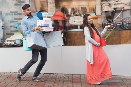 A pregnant woman with a man walking past the shop window with childrens goods.の写真素材