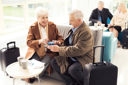 Elderly couple in the airport lounge. An elderly man makes an unexpected gift to an elderly woman.の写真素材