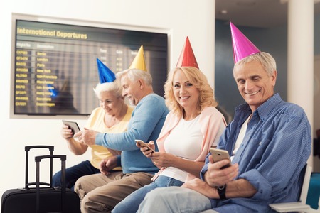 Elderly people celebrate their birthday in the waiting room at the airport. They put on holiday caps.の写真素材