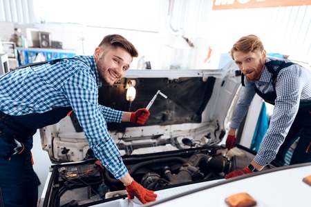 Father and son work at the auto service. Two mechanics work with the details of the car.の写真素材