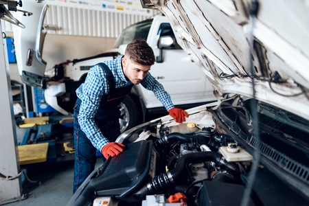 A young man works at a service station. The mechanic is engaged in repairing the car.の写真素材