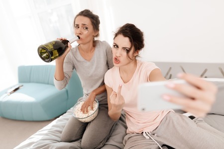 Girls are crying at the hen-party. They are sitting on the bed in room. The girls make selfie.の写真素材