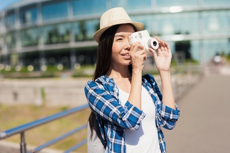 A girl is taking photos on a white camera. She has a bright hat on her head.の写真素材