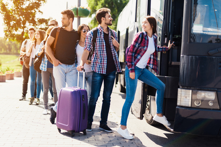 A group of tourists preparing to get on the bus. The guy with the girl goes into the bus and brings in their luggage.の写真素材