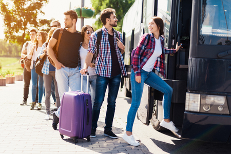 A group of tourists preparing to get on the bus. The guy with the girl goes into the bus and brings in their luggage.