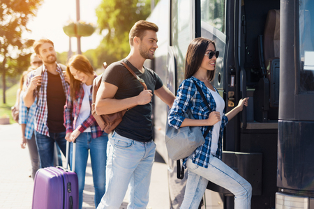 A group of tourists enters the bus. The guy and the girl are ready to sit down.