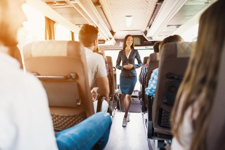A stewardess is posing on the bus. It stands between the rows of seats on which passengers are sitting.の写真素材