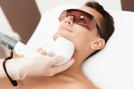 The man came to the procedure of laser hair removal. The doctor treats his neck and face with a special apparatus.の写真素材