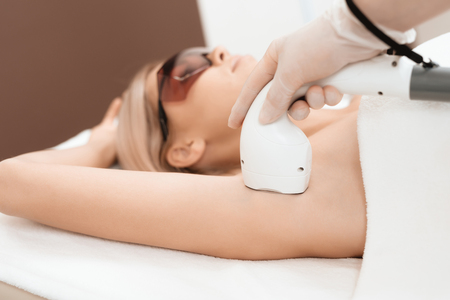 The woman came to the procedure of laser hair removal. The doctor treats her armpits with an apparatus.の写真素材