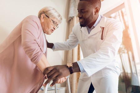 The doctor helps to get out of bed an elderly woman in a nursing home.の写真素材