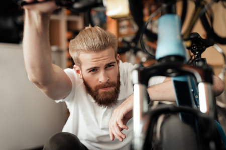 A young man with a beard looks at the details of the bicycle in the bicycle store.の写真素材